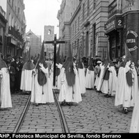 Nazarenos de la hermandad de San Benito en la esquina de la calle Almirante Apodaca con la plaza Cristo de Burgos. Al fondo, una empalizada cubre la fachada de la iglesia de Santa Catalina durante las obras de colocación de la portada gótica procedente de la iglesia de Santa Lucía. 1929. ©ICAS-SAHP, Fototeca Municipal de Sevilla, fondo Serrano