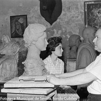 18.- El escultor e imaginero Antonio Illanes Rodríguez en su estudio modelando una obra con la  modelo de su inspiración al fondo. 1967. ©ICAS-SAHP, Fototeca Municipal de Sevilla, fondo Cubiles
