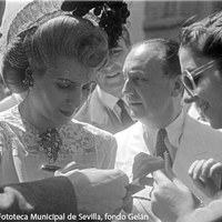 La expectación de la visita al barrio de la Macarena brindó imágenes como esta donde firma un autógrafo en presencia del alcalde Rafael Medina y el ministro de Justicia Raimundo Fernández Cuesta. ©ICAS-SAHP, Fototeca Municipal de Sevilla, fondo Gelán