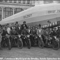 Celebración del Carnaval. Carroza del desfile representando el Graff Zeppelin en la trasera del actual Museo Arqueológico en la Plaza de América. La carroza lleva el nombre de la empresa de motocicletas “Triumph”. En la imagen, un grupo con motocicletas de la marca “Triumph” que participaron en el desfile. 28 de febrero de 1933 ©ICAS-SAHP, Fototeca Municipal de Sevilla, fondo Sánchez del Pando