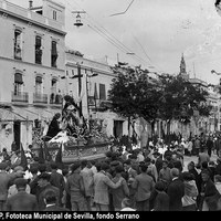 Paso de misterio del Cristo de la Misericordia y Nuestra Señora de la Piedad en la calle Adriano tras su salida de la capilla del Baratillo. Al fondo de la imagen se aprecia, bajo palio, a la Virgen de la Soledad que efectuaba su primera salida con la cofradía. En 1929 la virgen cambiaría su advocación por Caridad en su Soledad. En el paso de misterio aparecen las figuras arrodilladas de San Juan Evangelista y María Magdalena. 1926 ©ICAS-SAHP, Fototeca Municipal de Sevilla, fondo Serrano