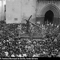 Salida procesional de la Hermandad de los Gitanos. Paso de Nuestro Padre Jesús de la Salud, con la túnica bordada, en la plaza de San Román. En la fachada de la iglesia un cartel hace alusión a la Exposición retrospectiva de arte concepcionista" con motivo del tercer centenario del voto concepcionista. Los nazarenos llevan aún la túnica blanca de cola recogida con esparto y el antifaz negro. 1918 ©ICAS-SAHP, Fototeca Municipal de Sevilla, fondo Serrano