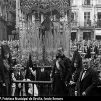 El palio de la Virgen de la Esperanza Macarena ante el palco de la Plaza de San Francisco presidido por el alcalde de la ciudad, Nicolás Díaz Molero, el Comisario de la Exposición Iberoamericana, José Cruz Conde y las concejalas María Luisa Seras y Diana García de Pesquera. La cofradía había retrasado su salida hasta la mañana del Viernes Santo debido a la lluvia de la madrugada. 1928 ©ICAS-SAHP, Fototeca Municipal de Sevilla, fondo Serrano