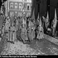 Hermandad de San Bernardo. Niños nazarenos del Cristo de la Salud en la calle Granada. A fondo, la Real Audiencia que ya aparece rehabilitada tras el incendio de 1918. Fachada pintada con el rojo almagre que proyectó Aníbal González (1924). La fachada se pintaría en blanco en 1929. A la izquierda, con pantalón corto, el hijo del fotógrafo. 1924-1928 ©ICAS-SAHP, Fototeca Municipal de Sevilla, fondo Serrano